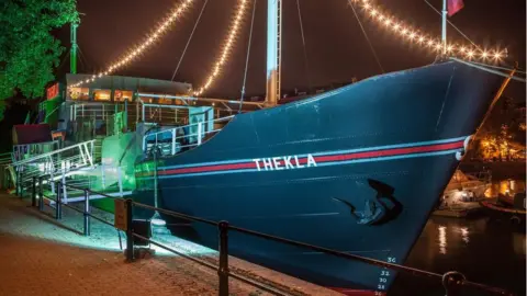 Thekla seen from the outside at night with string lights hanging from it