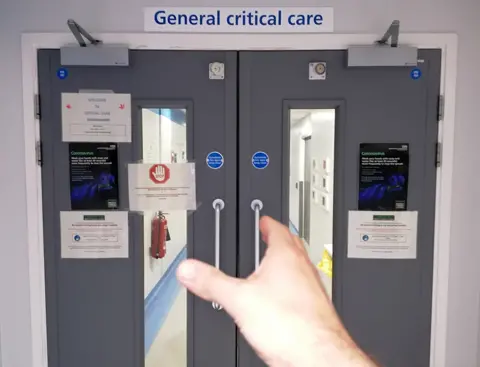  Joan Pons Laplana A hand reaches out to open the door of General Critical Care ward in a hospital