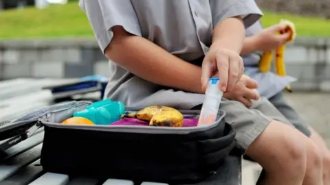 Getty Images Young boy with a packed lunch takes out his anaphylaxis auto injector