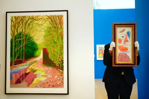 Victoria Jones/PA A gallery assistant holds a David Hockney 'Self Portrait' 1986 at Phillips in London, 14 September 2023
