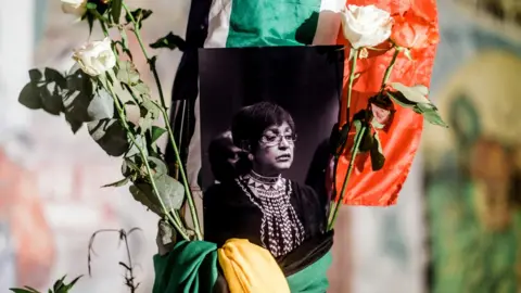 AFP A black and white photograph of the late Winnie Madikizela-Mandela is surrounded by the South African and African National Congress (ANC) flags on a pole at the Old Durban Prison's Human Rights wall as South Africans gather to pay respect to the late high-profile anti-apartheid activist during a candle vigil in Durban on April 2, 2018.