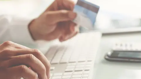 courtneyk Man holds a credit card while typing on a computer keyboard