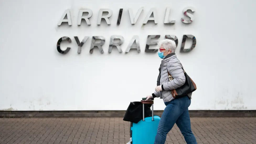 Getty Images Woman in mask walking past arrivals sign at Cardiff Airport