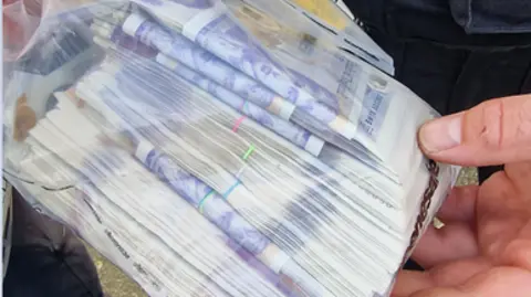 Merseyside Police A police officer holds a plastic bag full of £20 notes