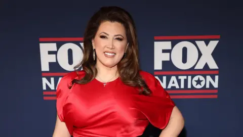 Getty Images A dark haired woman in a red dress in front of a banner saying "Fox Nation"