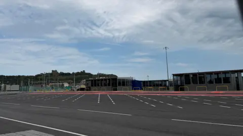 A large concrete area with low rise buildings / kiosks and lines for queues of cars.