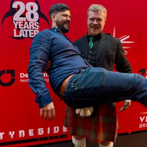 RuMac Ruairidh, who is wearing a kilt and Highland dress jacket, capers about with friend and fellow musician Ruairidh Graham, who wears a blue shirt and jeans.