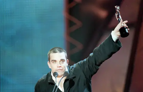 Getty Images Robbie Williams holding up a Brit award trophy