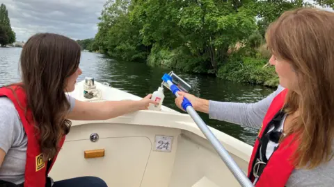 BBC Frances Mateo pours a river water sample into a container held by Izzy Wittrock on a boat