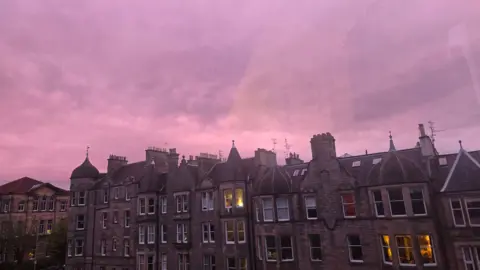 Sarah Grossman A bright purple sky above a row of flats in a big city 