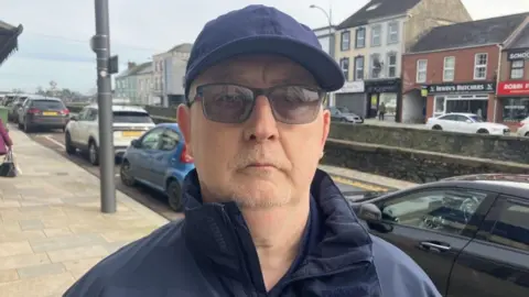 Kevin Barry, a man wearing a blue cap and blue jacket, who has dark glasses on his head.