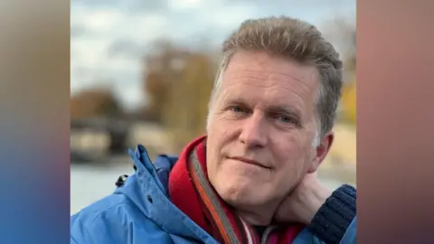 Charles Allen Charles Allen smiles at the camera with one hand resting on the back of his neck. He has short grey hair and wears a blue rain coat and red scarf.