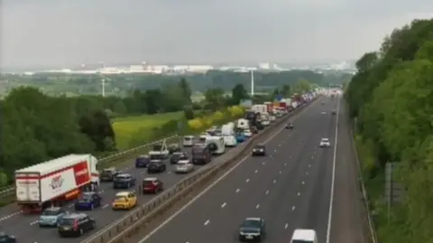 An image taken from a motorway camera shows long queues of traffic on the left hand side in all three lanes. The right hand side, travelling south, has only a few cars.