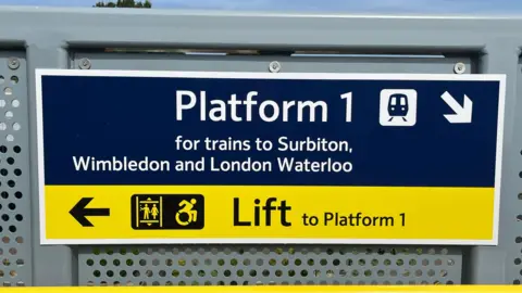 BBC/Julia Gregory A sign pointing to Platform 1 for trains to Surbition, Wimbledon and London to the right and pointing to the left for the lift