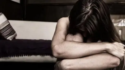 Getty Images A woman is crouched down and curled up in a ball. She seems scared and upset. 