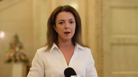 PA Media Northern Ireland's Infrastructure Minister Liz Kimmins, with long brown hair, wearing a white shirt. 