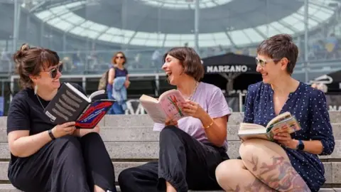 The Forum Three women reading books and laughing on the steps of The Forum in Norwich