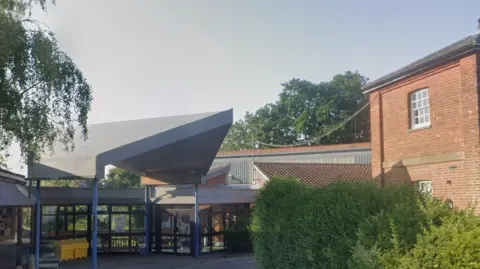 A view of the main entrance of the Dorking Community Hospital, a red brick and grey concrete and glass modern building.