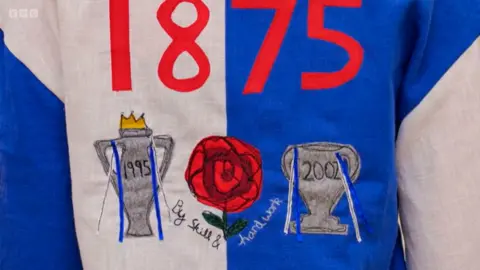 Close up of the back of the Blackburn Rovers-themed bowling shirt which features the club's iconic blue-and-white halved design, with a red rose crest on the front chest. The sketch shows both front and back views, with notes highlighting linen fabric, free-motion embroidered details, and appliquéd trophies and the year “1875” on the back.