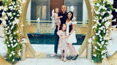 Family handout Chris and Lauren Capstick are posing in the middle of a flower arch with their two daughters. 
