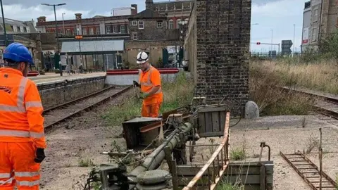 Lowestoft Central Project Two Network Rail workers wearing orange high visibility suits and helmets are dismantling old signal equipment close to railway lines at the station