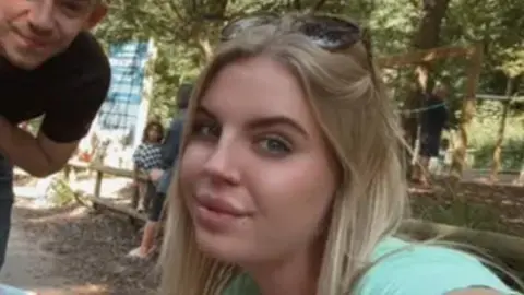 Ellie Howells pictured wearing a black dress with white hearts. Ellie has blonde hair and black-rimmed glasses.