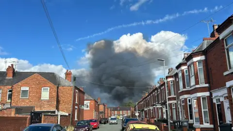 BBC Plumes of dark grey smoke rise from behind a street of red-brick houses