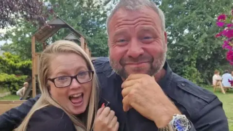 A woman with blonde hair and black glasses alongside a man in a blue shirt.