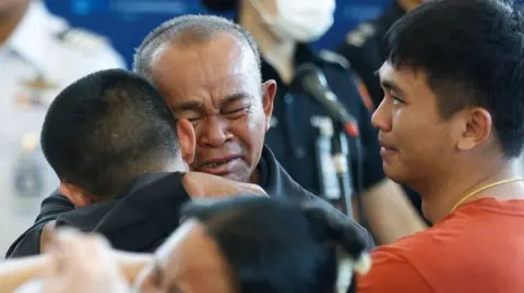 Thai hostage Pongsak Thaenna (L), who was taken in the attack led by the Palestinian militant group Hamas on 07 October 2023, is embraced by his father (C) next to his younger brother (R)