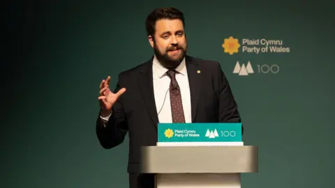 Matthew Horwood/Plaid Cymru Luke Fletcher stood at Plaid Cymru conference in front of a lectern dressed with the party logo.