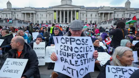 Reuters Protesters hold placards during a mass demonstration organised by Defend our Juries, against the British government's ban on Palestine Action.