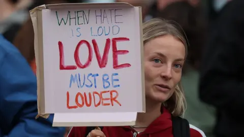 PA Media Local businesses west London also closed up earlier as extra police were deployed across the capital. One woman in Brentford held up a sign denouncing hatred in society