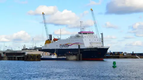 BBC A wide shot of Commodore Goodwill entering a harbour. It is big a white, with a navy blue underside.