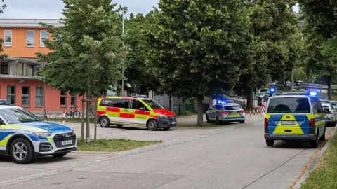 AFP via Getty Images Emergency service vehicles with flashing lights outside a school building, the road is quiet.