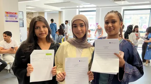 BBC/ Julia Bryson Three teenage girls stand together holding pieces of white paper