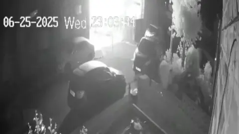 A black and white still from a security camera shows a terraced house engulfed in a ball of bright light moments before it exploded.