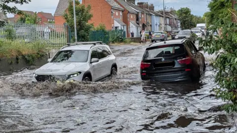 A white Mercedes and a black BMW attempting to drive through flood water in Ipswich.