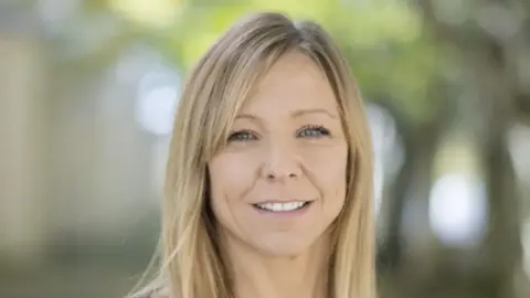 A headshot of Claire Chick who is smiling at the camera. The background is blurred.
