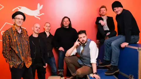 Peatbog Faeries Members of the Peatbog Faeries pictured against a red backdrop.