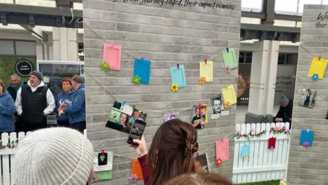A "memorial wall" - it consists of MDF boards with a printed overlay which looks like grey bricks. On it are spaces for people to hang photos of their loved ones off strings. It is situated in the atrium of a shopping centre.