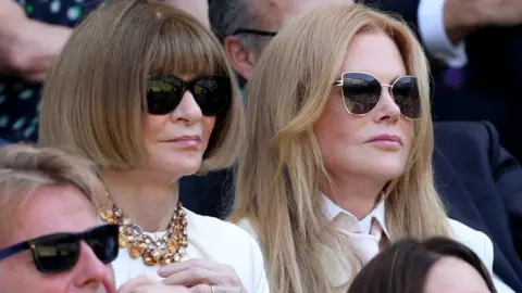 Anna Wintour and Nicole Kidman, both wearing dark glasses, watch a tennis match