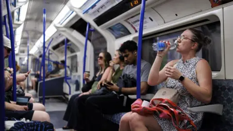 EPA/Shutterstock The inside of a Tube carriage with passengers sitting down. The women closest to the camera is drinking a bottle of water. 