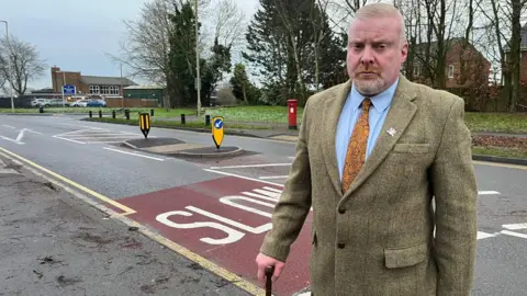 A man wearing a green blazer in front of a road in Tipton