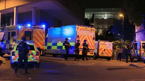 PA Media Emergency services vehicles are stationed outside the Manchester Arena following the attack. A number of armed police officer are patrolling the area.