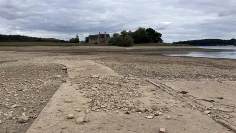 BBC/Ben Jackson The reservoir is largely empty with concrete and stones on show. A small amount of water can be seen in the distance. 