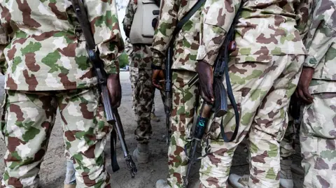 Nigerian soldiers, in camouflage uniform, from the Multinational Joint Task Force (MNJTF) hold Kalashnikovs at the MNJTF military base