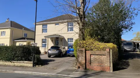 The front of a cream coloured building with two cars parked outside