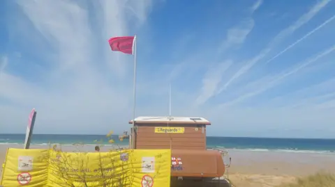 BBC A picture of a beach with a large red flag flying.