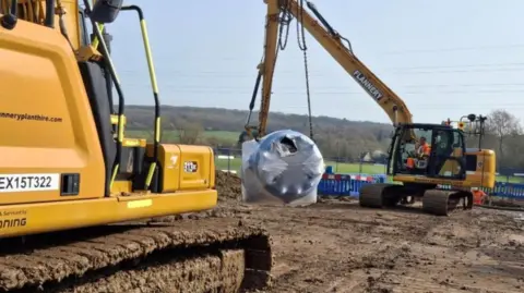 Thames Water Muddy field with two large diggers, one has a piece of equipment in a chain cradle to fix a burst water main.
