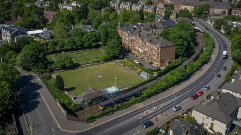 Campbell Ramage An aerial view of a bowling green with a block of flats and a motorway road running alongside it.